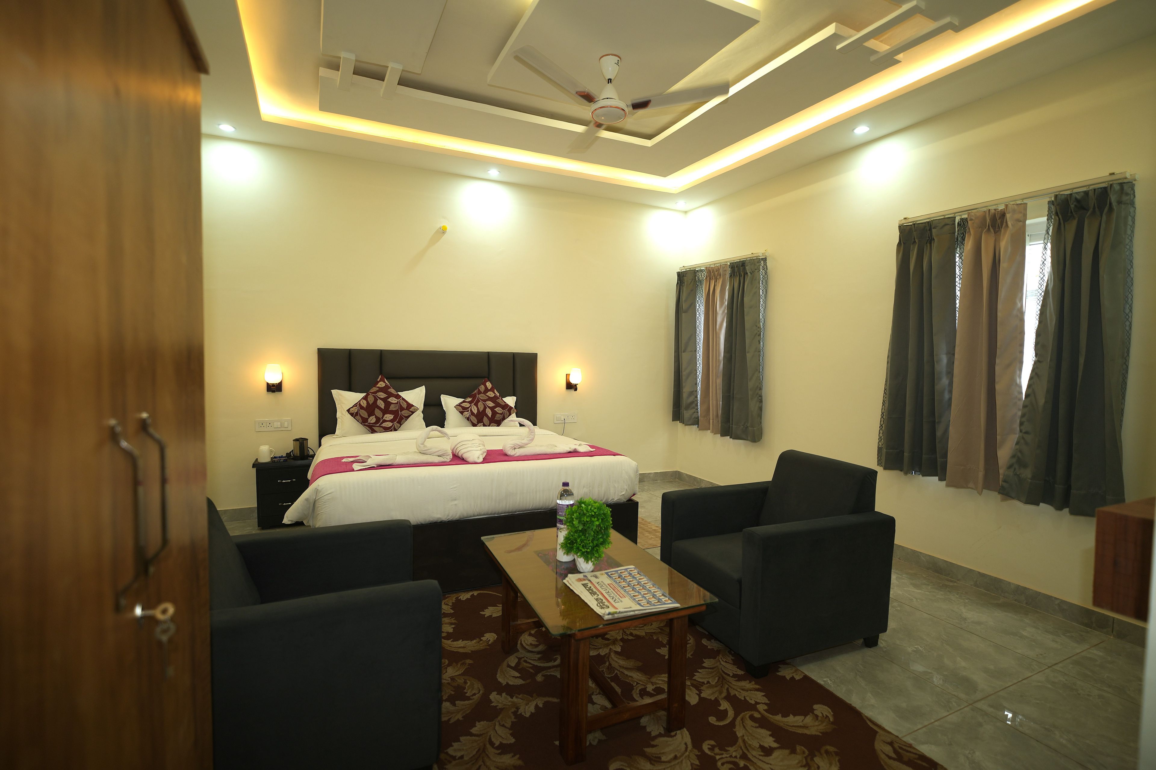A hotel room with a bed, two armchairs, a coffee table, and a window with curtains.