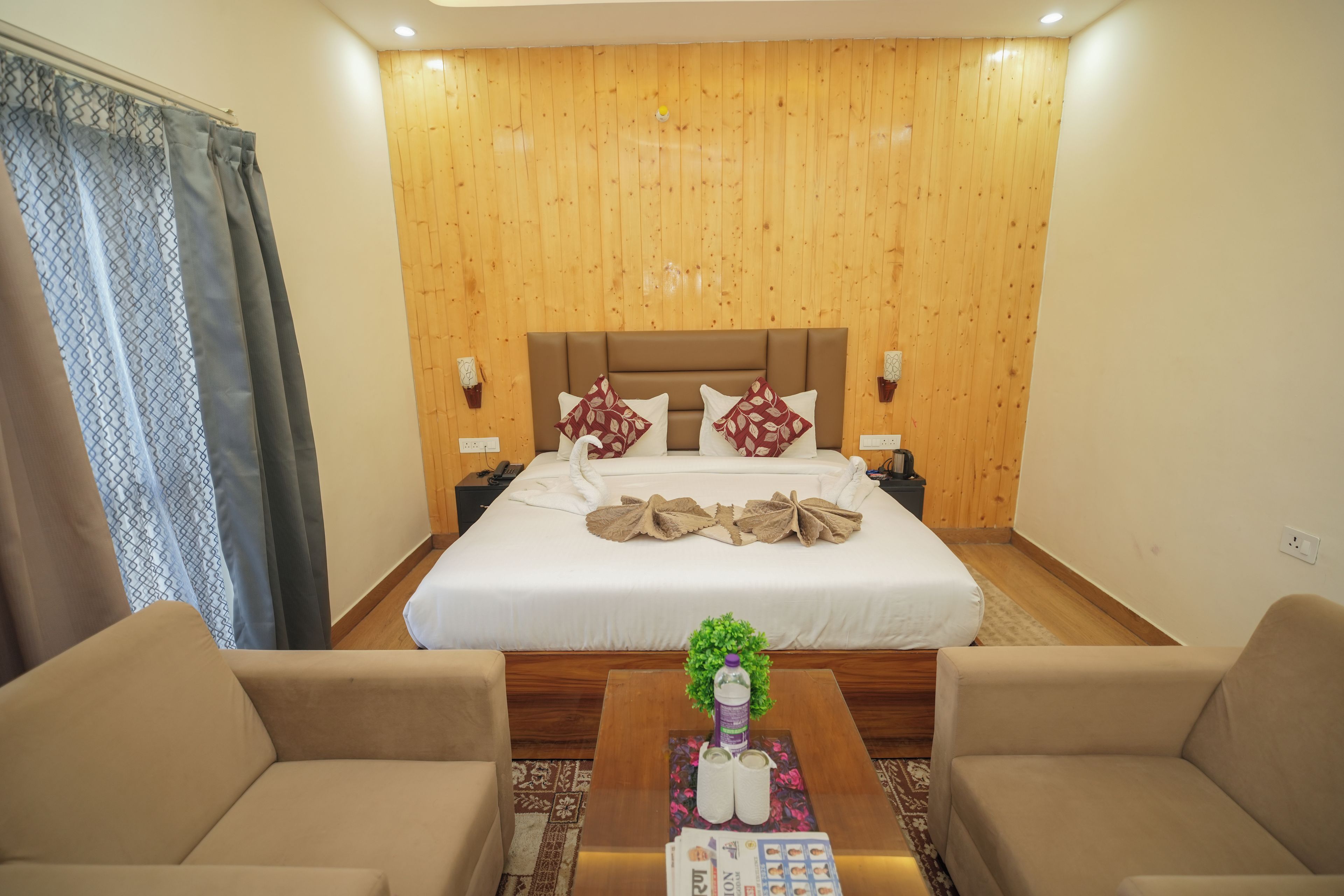 A hotel room with a large bed, two bedside tables, a coffee table with a plant, and two armchairs.