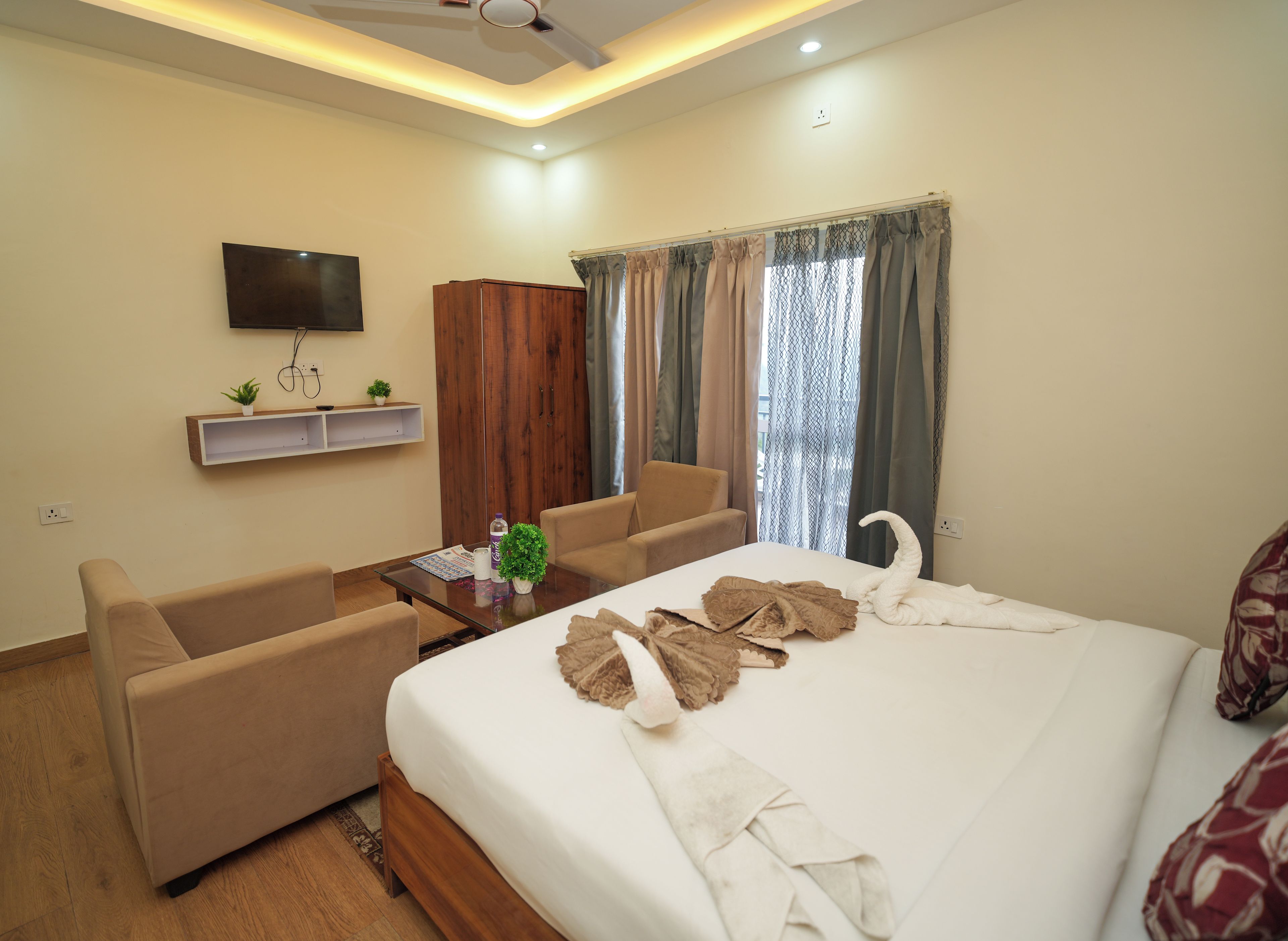 A hotel room with a bed, two sofas, a television, a wardrobe, and a window with curtains.