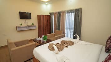A hotel room with a bed, two sofas, a television, a wardrobe, and a window with curtains.