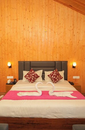 A hotel room with a wooden paneled wall, a bed with white bedding, two decorative pillows, a bedside table with a lamp, and a nightstand with a phone.