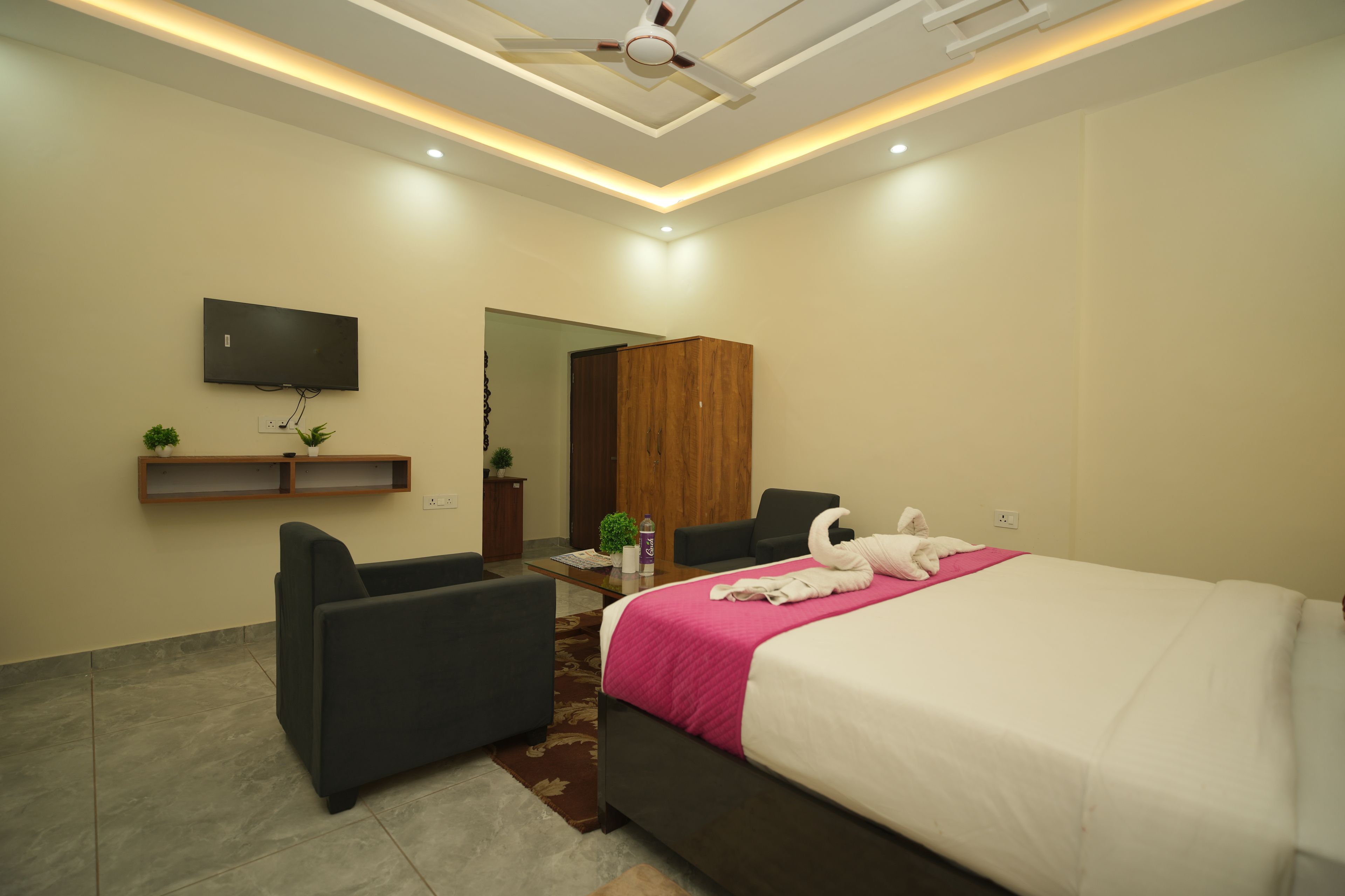 A hotel room with a bed, a desk, a chair, a TV mounted on the wall, and a ceiling fan.