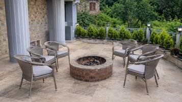 Un área de estar al aire libre con sillas de mimbre y una chimenea central.