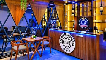 A cafe interior with wooden furniture, a counter with a neon sign, and hanging plants.