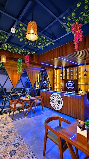 Interior de una cafetería con muebles de madera, una barra con letrero de neón y plantas colgantes.