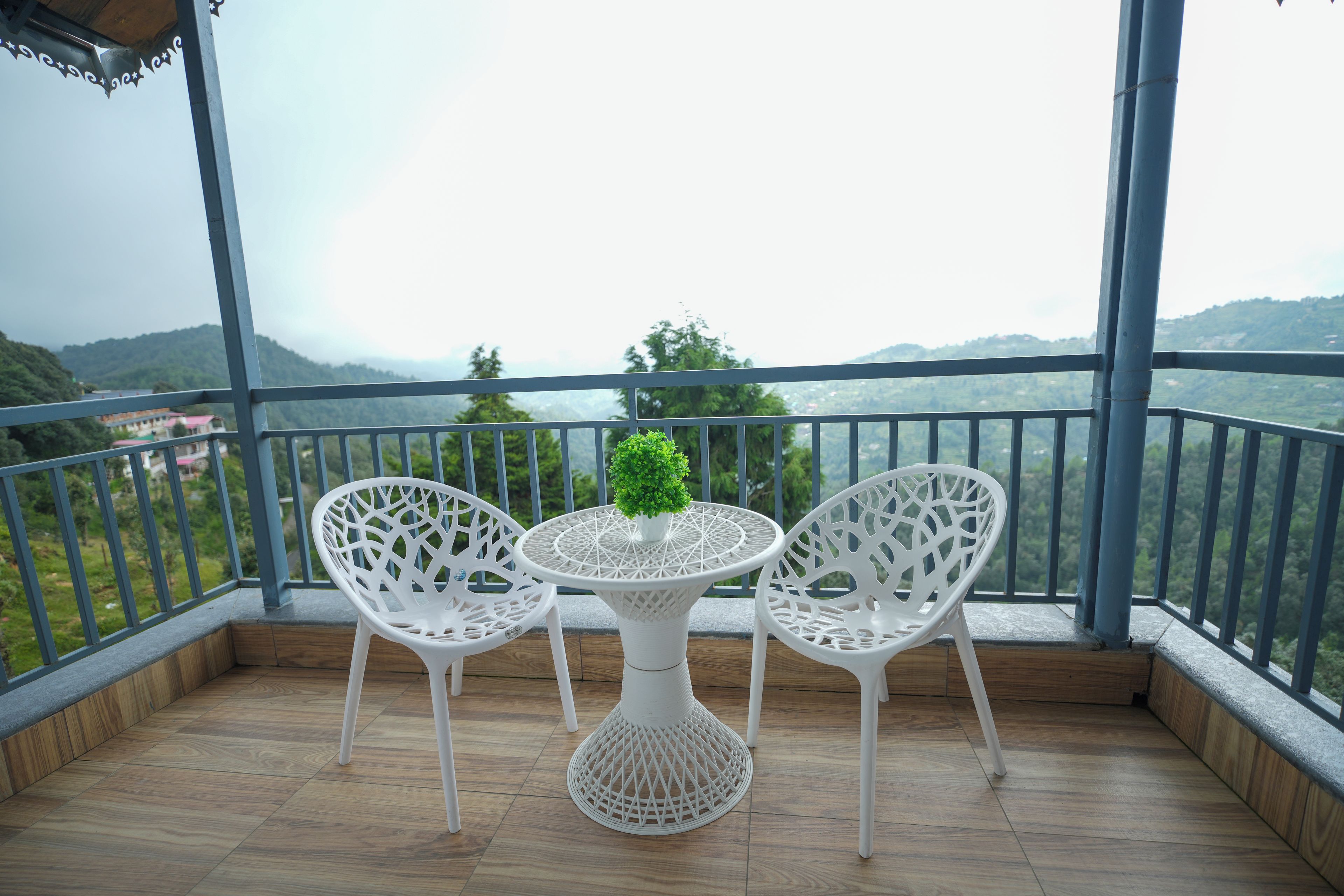 A balcony with two white chairs and a table, overlooking a mountainous landscape.
