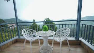 A balcony with two white chairs and a table, overlooking a mountainous landscape.