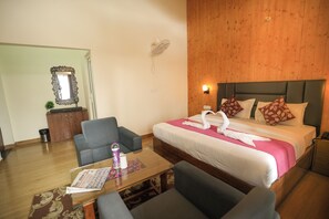 A hotel room with a bed, a sofa, a table, a mirror, and a wall-mounted fan.