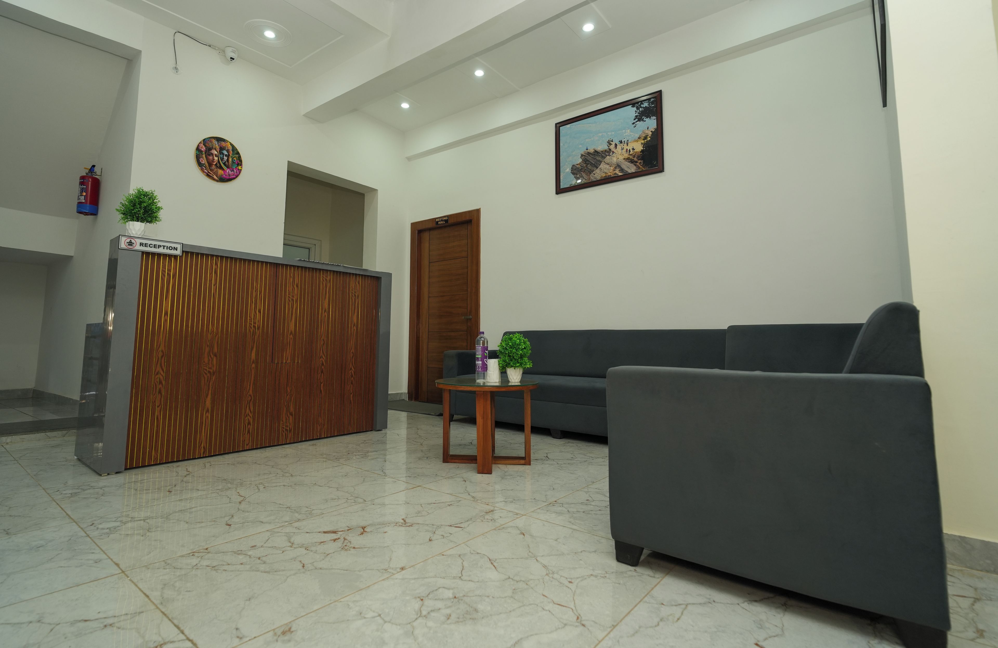 A reception area with a reception desk, a sofa, a small table with a plant, and a framed picture on the wall.