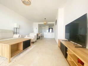 A modern living room with a sofa, a coffee table, a TV, and a dining area in the background. - Luxury 2-Bedroom Apartment in El Higuerón (Fuengirola)