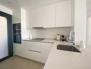 A modern kitchen with white cabinets, a stainless steel sink, and a built-in oven. - Luxury 2-Bedroom Apartment in El Higuerón (Fuengirola)