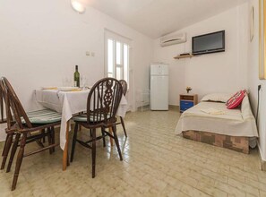 Ein gemütlicher Raum mit Esstisch, Stühlen, einem Bett, einem Fernseher und einem Kühlschrank.