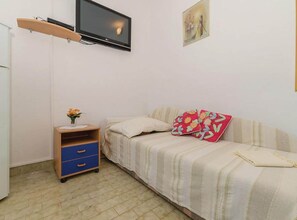 Ein Schlafzimmer mit einem Bett, einem kleinen Nachttisch mit Blumenvase, einem an der Wand montierten Fernseher und einem Wandbild.
