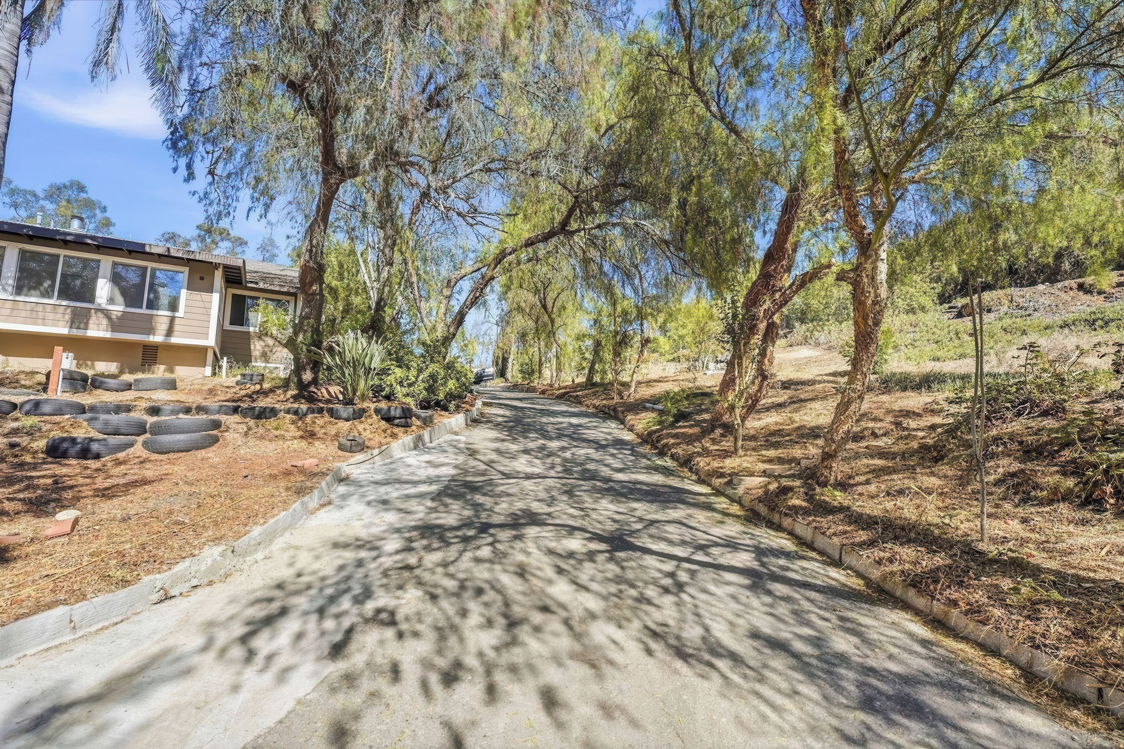 A residential property with a paved driveway, surrounded by trees and a hillside.