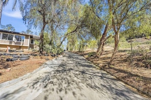 Propiedad residencial con entrada pavimentada, rodeada de árboles y una ladera.