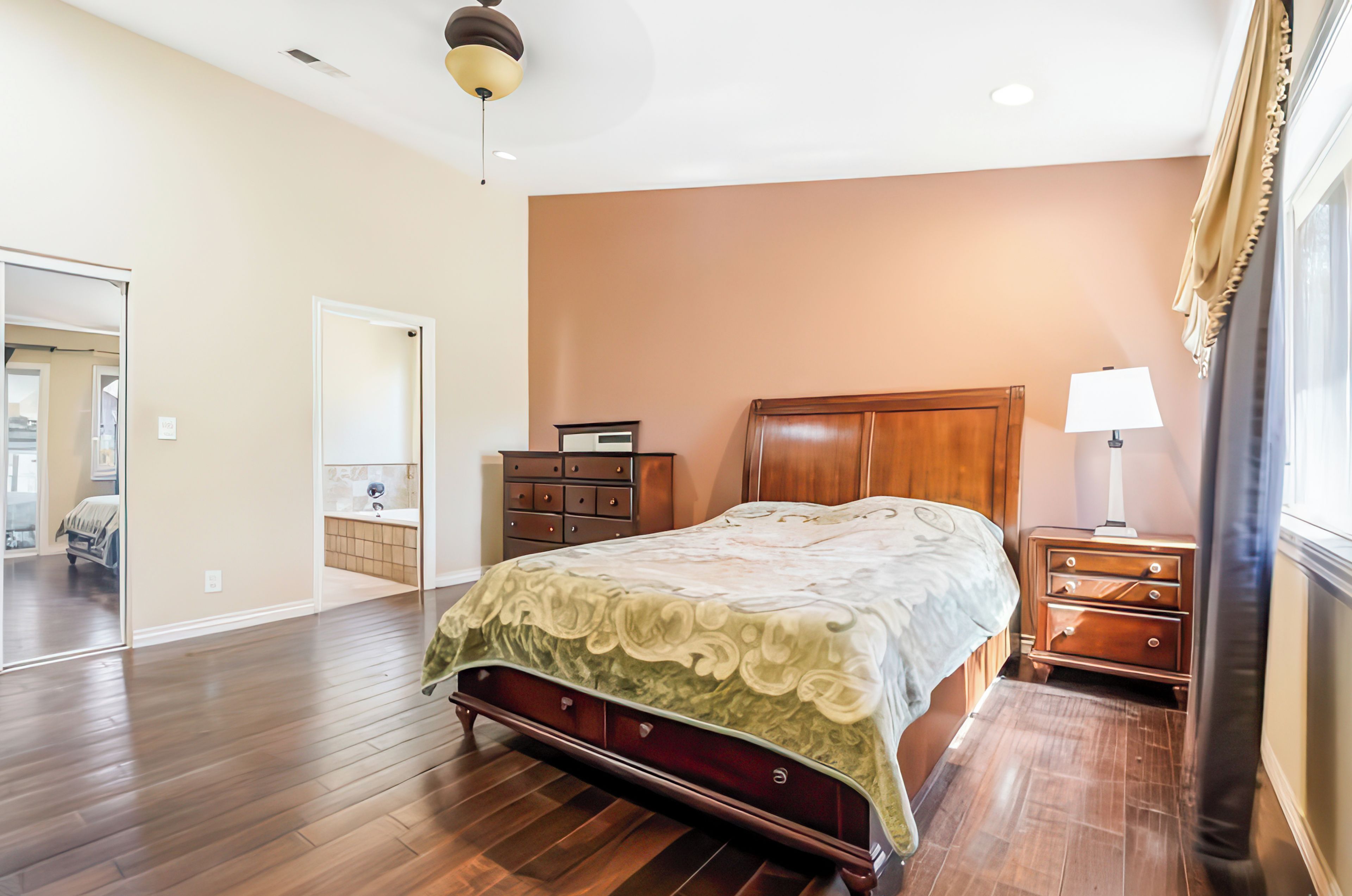 A bedroom with a wooden bed, a dresser, a nightstand, and a ceiling fan.