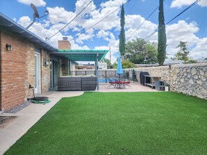 Un patio trasero con terraza, zona de estar cubierta y una parrilla.