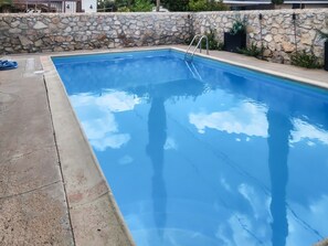 Una piscina rectangular con pared de piedra y escalera metálica.