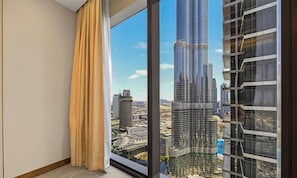 A room with a large window overlooking a cityscape, featuring a prominent skyscraper. - Downtown Icon Living | Address Opera 3BR (Dubai)