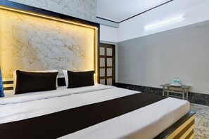 Habitación de hotel con una cama grande, cabecera de mármol, mesita de noche con botellas de agua y vistas al exterior.