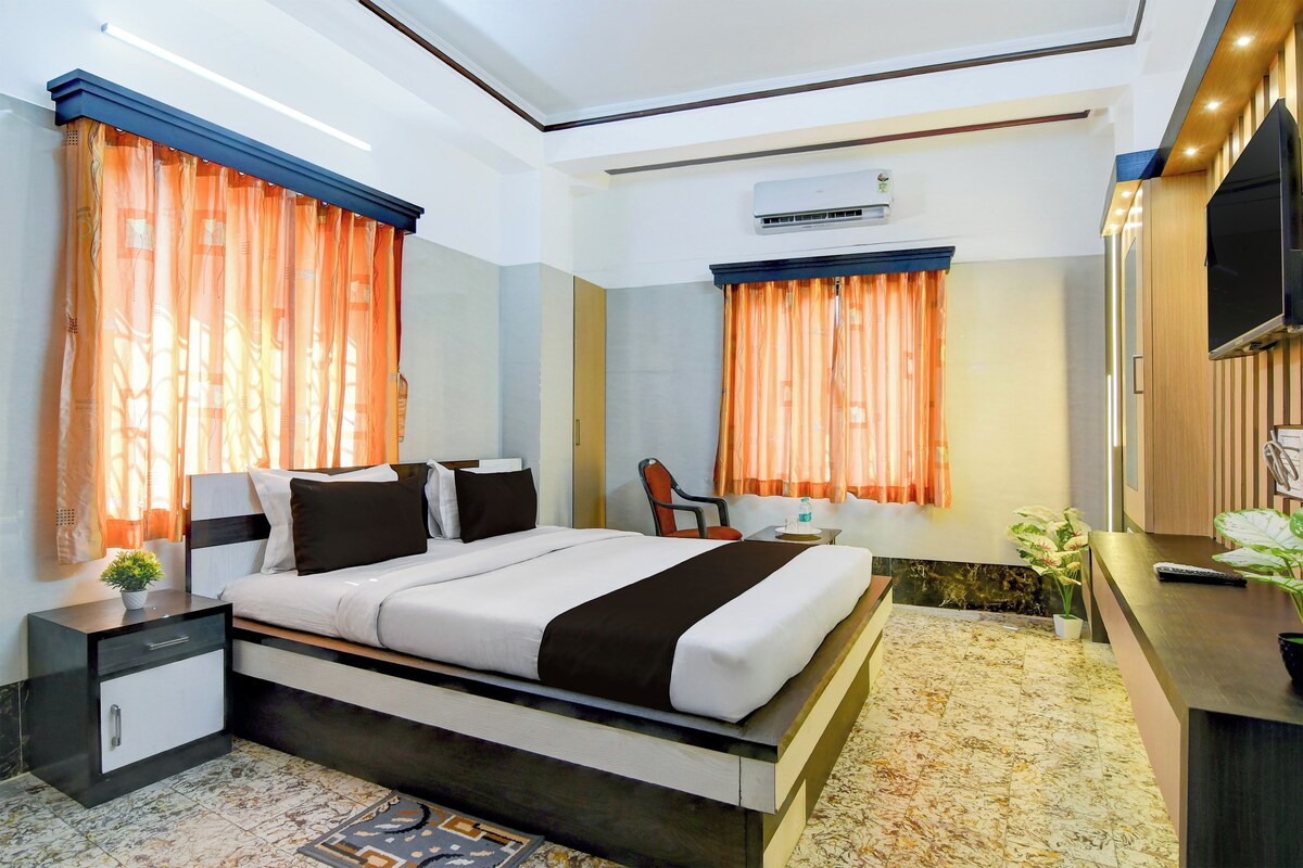A hotel room with a bed, bedside tables, a desk, an air conditioning unit, and a TV.