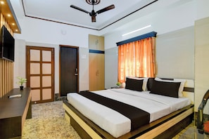 Une chambre d’hôtel avec un lit, un bureau, un ventilateur de plafond et une fenêtre avec des rideaux.