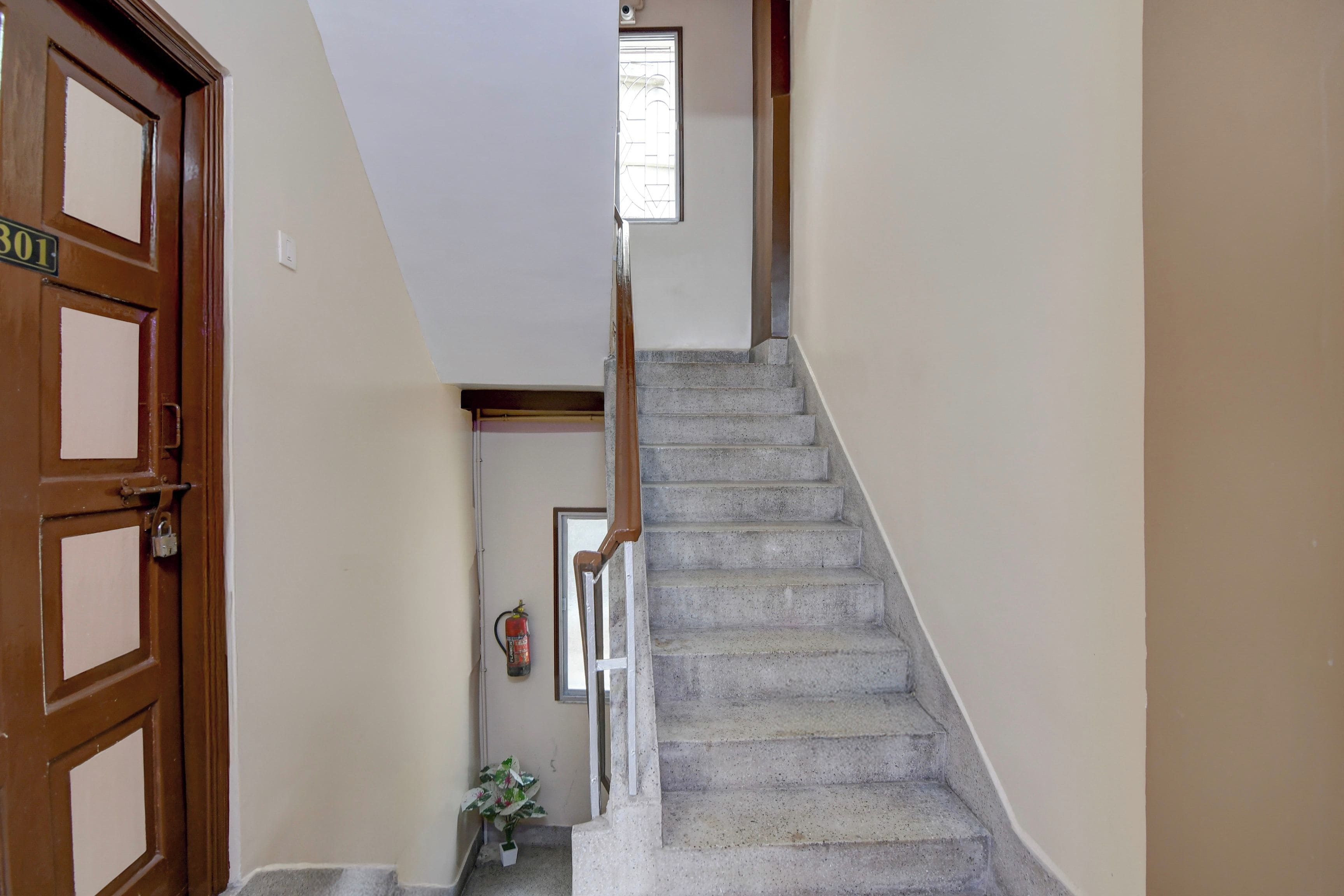 Una escalera con barandilla que lleva a un piso superior, una puerta con placa de número y una planta pequeña en la parte inferior.