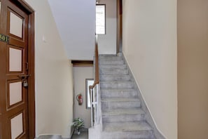Una escalera con barandilla que lleva a un piso superior, una puerta con placa de número y una planta pequeña en la parte inferior.
