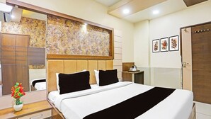 Una habitación de hotel con una cama grande, un cabecero de madera, un espejo, una mesita de noche con una lámpara y una pared decorada con obras enmarcadas.