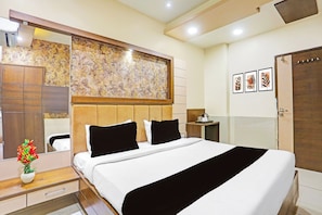 Ein Hotelzimmer mit einem großen Bett, einem hölzernen Kopfteil, einem Spiegel, einem Nachttisch mit Lampe und einer Wand mit gerahmten Kunstwerken.