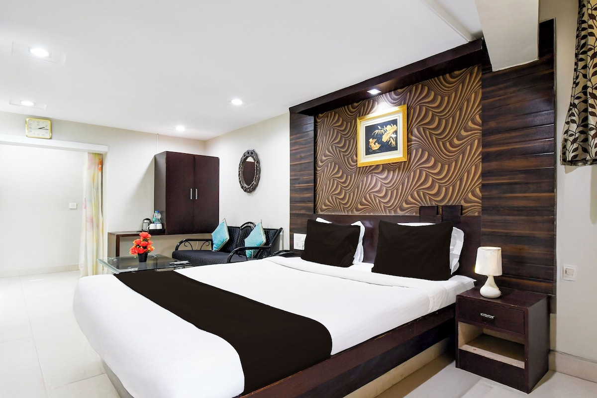A modern bedroom with a large bed, a bedside table, a desk, a chair, a mirror, and a clock on the wall.