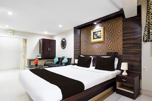 A modern bedroom with a large bed, a bedside table, a desk, a chair, a mirror, and a clock on the wall. - Hotel O Raipur formerly Hotel Okasu (Raipur)