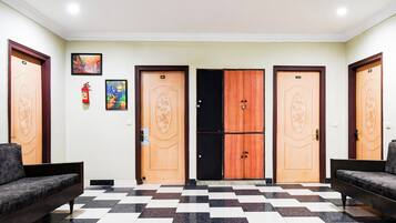 A lobby with checkered flooring, two sofas, and three doors with numbers.