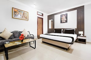 A modern bedroom with a bed, a sofa, a coffee table with a vase of flowers, and two framed pictures on the wall. - Hotel O Raipur formerly Hotel Okasu (Raipur)