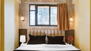 A hotel room with a bed, two bedside lamps, a window with a view, and a floral wallpaper design. - Collection O Veerbhadra Nagar Baner (Pune)