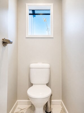 A bathroom with a toilet, a window with a view of the sky, and a door. - Coastal 3-bed Haven With Panoramic Views (Portarlington)