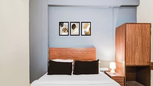 Ett hotellrum med en säng, två kuddar, ett sängbord med en lampa och en garderob i trä.