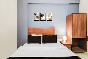 A hotel room with a bed, two pillows, a nightstand with a lamp, and a wooden wardrobe. - Hotel O Paradise Circle (Hyderabad)