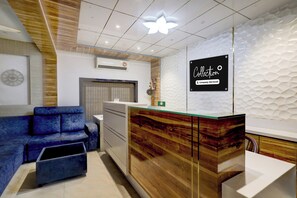 A reception area with a wooden reception desk, a blue sofa, and a decorative wall. - Collection O Chidambaram Stadium (Chennai)