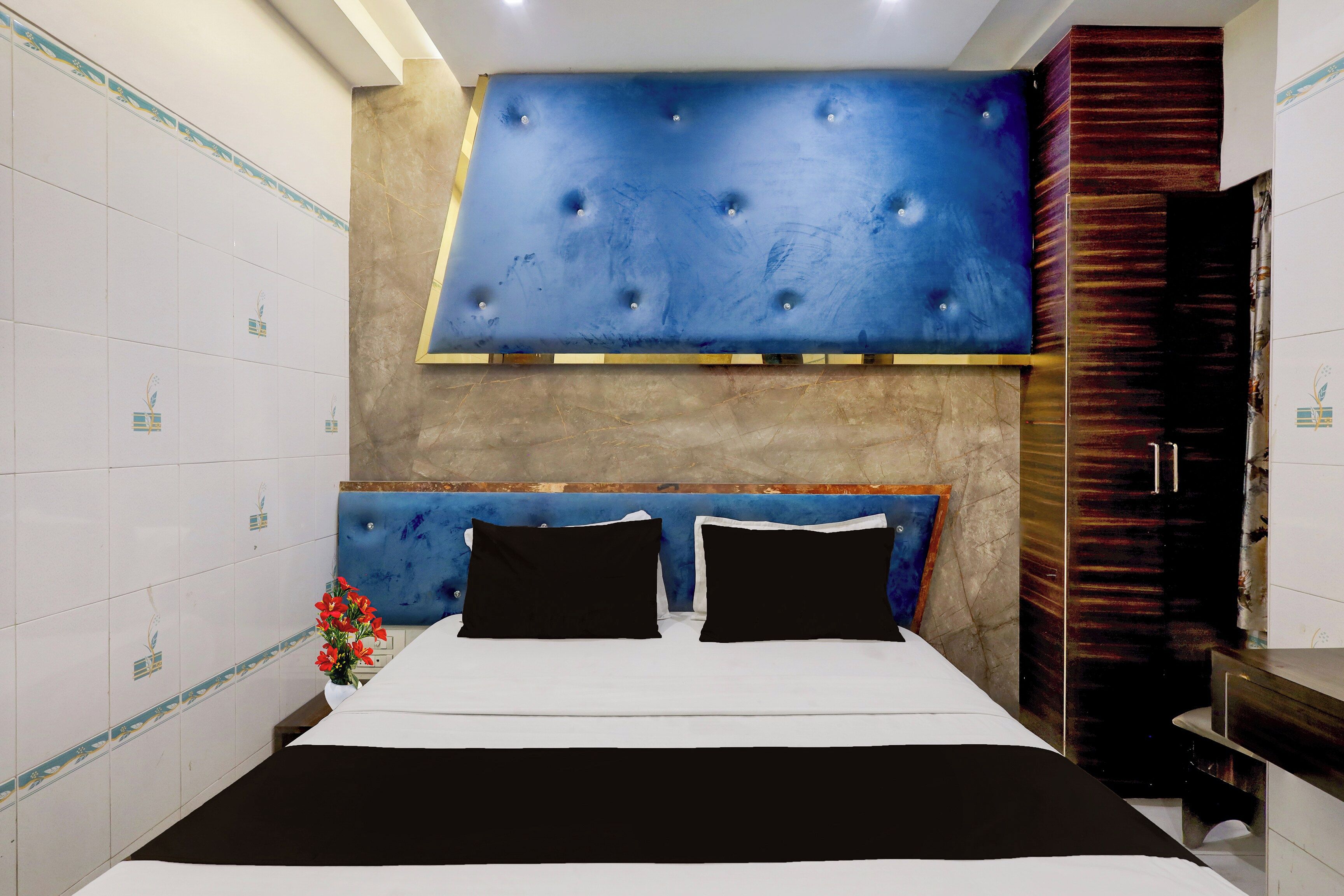 A bedroom with a bed, a blue headboard, a wooden wardrobe, and patterned tiles.