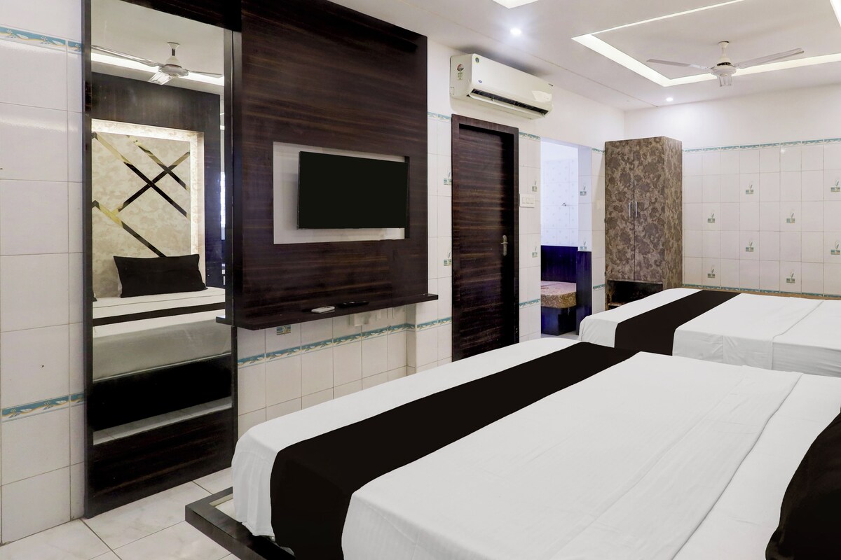 A hotel room with two beds, a flat-screen TV, an air conditioning unit, a ceiling fan, and a large mirror.