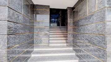 Escadaria com paredes de mármore e detalhes dourados, que leva a um interior escuro.