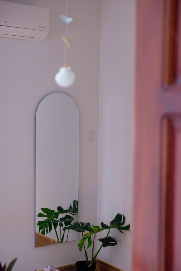 A bathroom with a mirror, a potted plant, and an air conditioning unit.