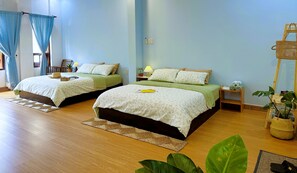 A hotel room with two beds, a wooden floor, a small table with a lamp, and a potted plant.