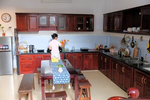 A kitchen with wooden cabinets, a refrigerator, a dining table with benches, and a clock on the wall.