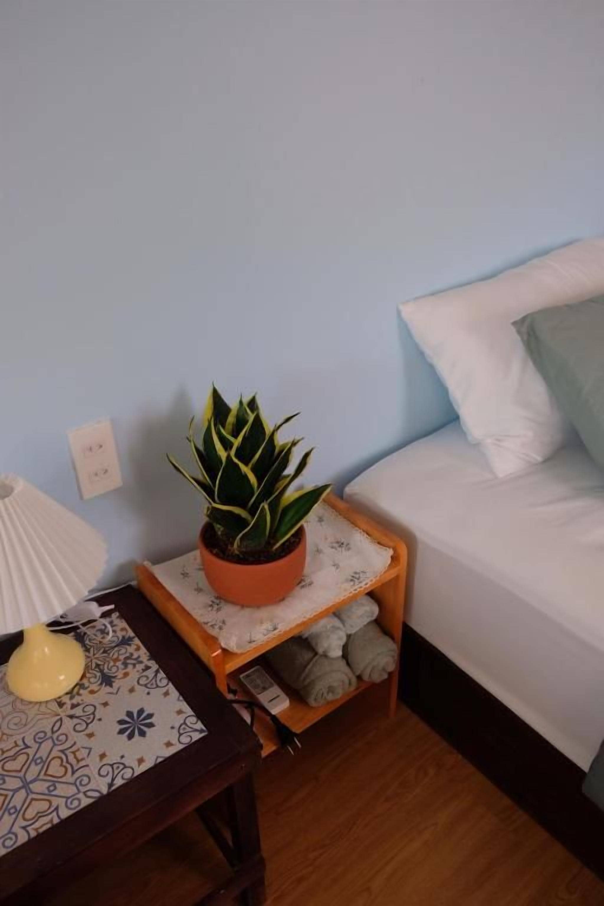 Une petite table de chevet avec un pot de plante, une lampe et une étagère pour les serviettes pliées.