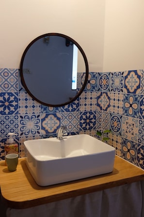 A bathroom with a white sink, a round mirror, and blue patterned tiles. - Ruhome Quy Nhon - Central & Near Beach (Quy Nhon)