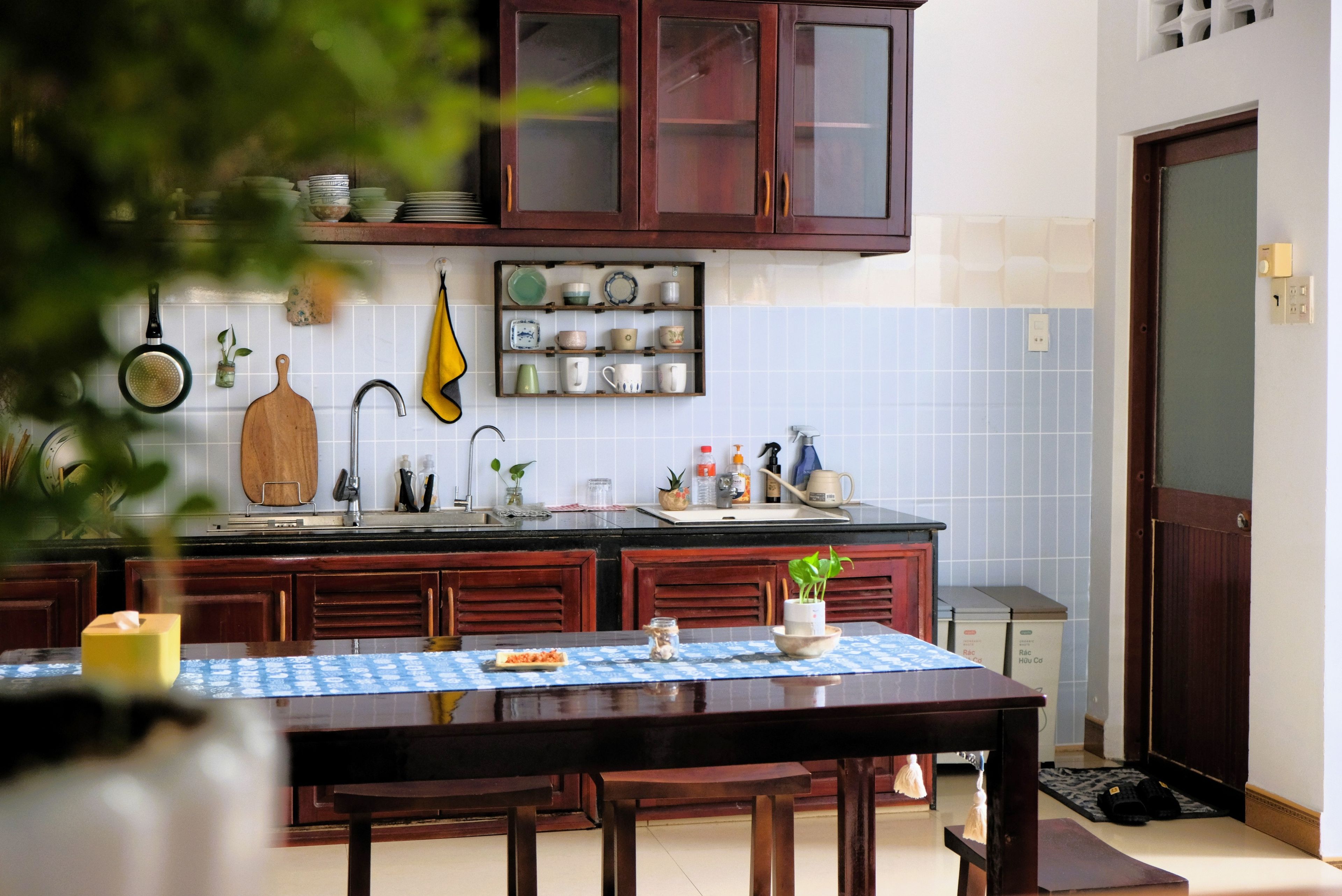 Uma cozinha com armários de madeira, painel de azulejos e uma mesa de jantar com toalha azul.