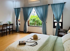 A bedroom with a bed, curtains, a desk, and a window with a view of greenery. - Ruhome Quy Nhon - Central & Near Beach (Quy Nhon)