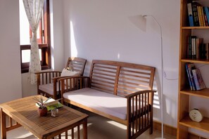 A room with a wooden sofa, a small table with a plant, a bookshelf with books, and a window with curtains. - Ruhome Quy Nhon - Central & Near Beach (Quy Nhon)